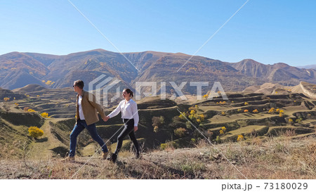 Couple runs along hill with dry grass against cascade slope Couple runs along hill with dry grass against cascade slope 73180029