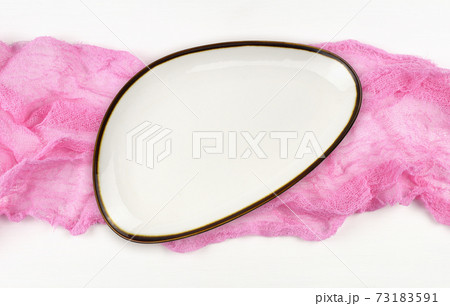 Empty white plate on pink folded cotton textile on white painted wooden table Empty white plate on pink folded cotton textile on white painted wooden table 73183591