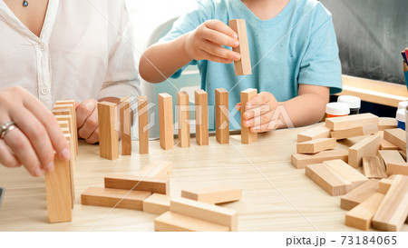 Boy pushing wooden block and starting domino effect. Wooden blocks falling in chain. Concept of children education at home during lockdown and staying at home Boy pushing wooden block and starting domino effect. Wooden blocks falling in chain. Concept of children education at home during lockdown and staying at home 73184065