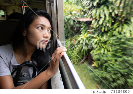 A young woman goes by train and looks out the window. 73184809