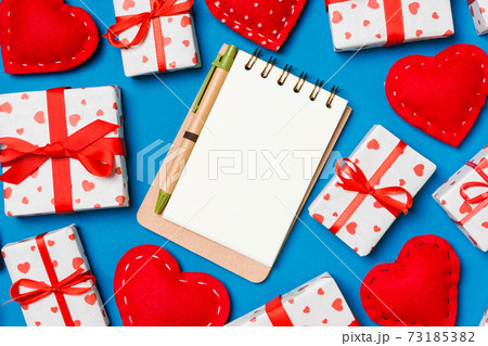 Holiday composition of notebook, gift boxes and red textile hearts on colorful background with empty space for your design. Top view of Valentine's Day concept 73185382