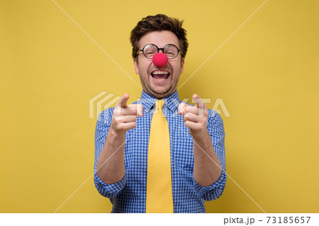Laughing young guy dressed lika a clown pointing with finger at camera. 73185657