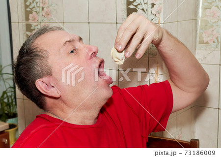 A man puts himself a dumpling with his hand in his open mouth A man puts himself a dumpling with his hand in his open mouth 73186009