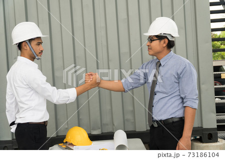 Two construction engineers finished working shaking hands outdoors in construction site.  73186104