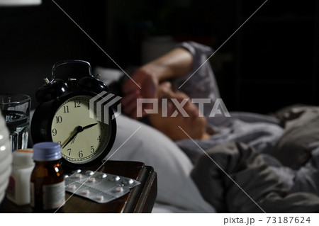 Depressed senior woman lying in bed cannot sleep from insomnia. Selective focus on alarm clock 73187624
