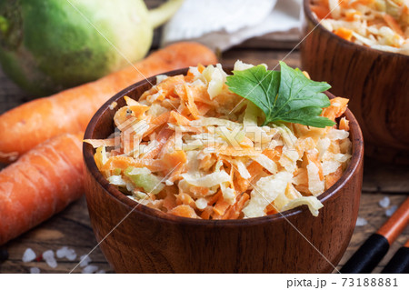 Salad of fresh grated carrots and green radish with sauce. Wooden table and dishes. 73188881