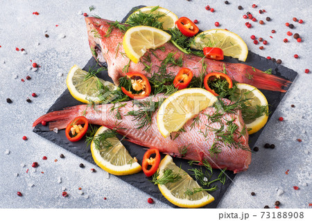 Raw fish perch without a head with lemon slices and dill greens and red hot chili peppers on a slate stand concrete background. Copy space. Healthy food and diet concept. Ingredients for cooking fish. Raw fish perch without a head with lemon slices and dill greens and red hot chili peppers on a slate stand concrete background. Copy space. Healthy food and diet concept. Ingredients for cooking fish. 73188908