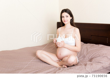 pregnant young woman sitting on bed and drinking coffee at home. maternity concept 73190656