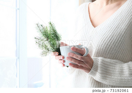 A Christmas tree in the hands of a girl in a white knitted sweater. Minimalism. Cozy winter, New Year. 73192061