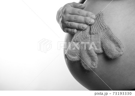Pregnant woman's tummy, she holds socks, white background, black and white photo Pregnant woman's tummy, she holds socks, white background, black and white photo 73193330