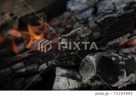 Smoldered logs burned in vivid fire close up. Atmospheric background with flame of campfire. Unimaginable detailed image of bonfire from inside with copy space. Whirlwind of smoke and glowing embers. 73193995