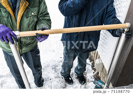 雪降りの中での玄関外階段手摺取り付け工事手すり棒組付けの写真素材