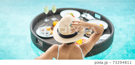 Happy woman in white swimsuit having Floating Breakfast tray in luxury pool hotel, young female with hat enjoy in tropical resort. Relaxing, Exotic summer travel, holiday, vacation and weekend 73204811