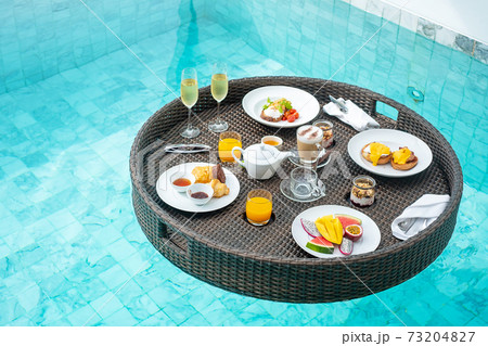 Floating Breakfast tray in swimming pool at luxury hotel or tropical resort villa, fruits; mango, watermelon dragon and passion fruit, food, bread, coffee, tea, wine and orange juice. Exotic summer Floating Breakfast tray in swimming pool at luxury hotel or tropical resort villa, fruits; mango, watermelon dragon and passion fruit, food, bread, coffee, tea, wine and orange juice. Exotic summer 73204827
