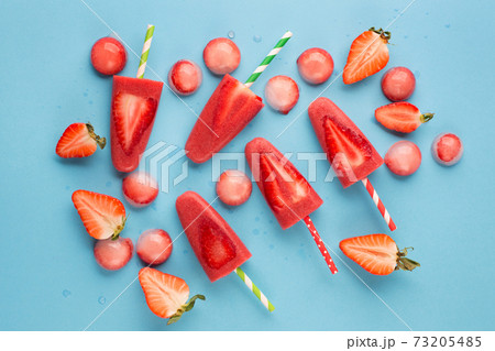 Delicious homemade strawberry popsicles with colorful sticks on blue backgound, top view. 73205485