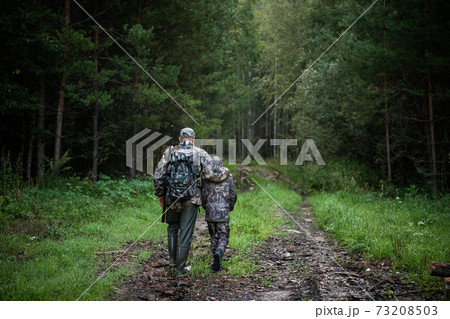 Hunters with hunting equipment going away through rural forest at sunrise during hunting season in countryside. 73208503