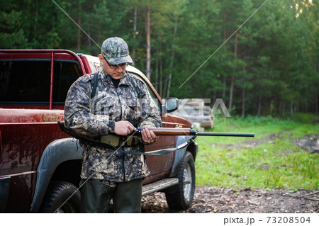 Man hunter standing with shotgun rifle near his car outdoor preparing for bird hunt in autumn forest 73208504