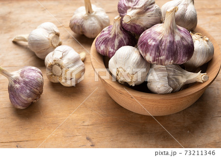 bunch of fresh garlic in a wooden plate on a brown table 73211346