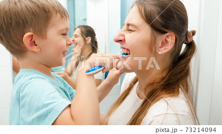 Funny toddler boy cleaning and brushing mothers teeth. Concept of family hygiene and teeth healthcare Funny toddler boy cleaning and brushing mothers teeth. Concept of family hygiene and teeth healthcare 73214094
