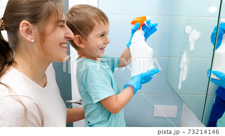 Happy smiling mother with little toddler son applying chemical detergent for washing and cleaning mirrors in bathroom. Family doing daily routine and housework Happy smiling mother with little toddler son applying chemical detergent for washing and cleaning mirrors in bathroom. Family doing daily routine and housework 73214146