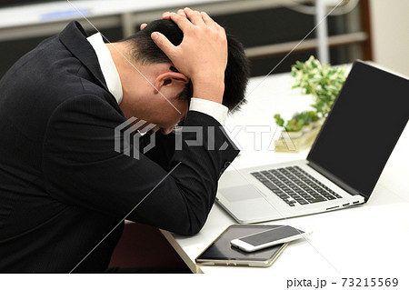 頭を抱えて悩むビジネスマンの男性のイメージ 73215569