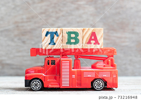 Red fire truck hold letter block in word TBA (abbreviation of to be announced)  on wood background 73216948