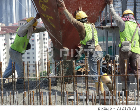 MALACCA, MALAYSIA -FEBRUARY 16, 2017: Group of construction workers pouring wet concrete using concrete bucket transported by tower crane into timber form work at the construction site. MALACCA, MALAYSIA -FEBRUARY 16, 2017: Group of construction workers pouring wet concrete using concrete bucket transported by tower crane into timber form work at the construction site. 73217973