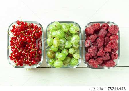 Assorted berries of raspberries, gooseberries and red currants in glass bowls on a white table. Assorted berries of raspberries, gooseberries and red currants in glass bowls on a white table. 73218948