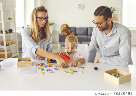 Focused mom, dad and toddler son play and compose words from scattered colored letters. Focused mom, dad and toddler son play and compose words from scattered colored letters. 73220492