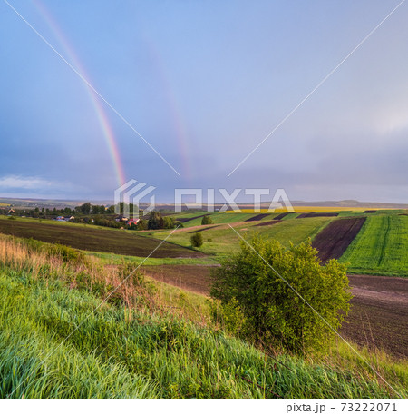 Spring rapeseed and small farmlands fields after rain evening view, cloudy sunset sky with rainbow and rural hills. Natural seasonal, weather, climate, eco, farming, countryside beauty concept. Spring rapeseed and small farmlands fields after rain evening view, cloudy sunset sky with rainbow and rural hills. Natural seasonal, weather, climate, eco, farming, countryside beauty concept. 73222071