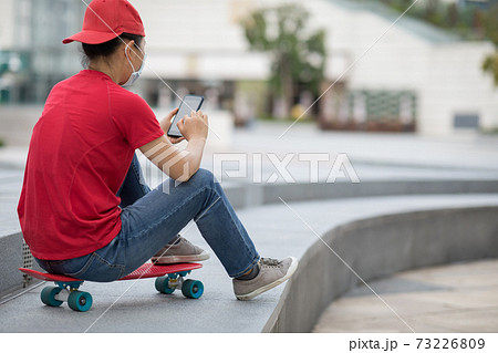 Asian woman sit on skateboard using smartphone in modern city 73226809