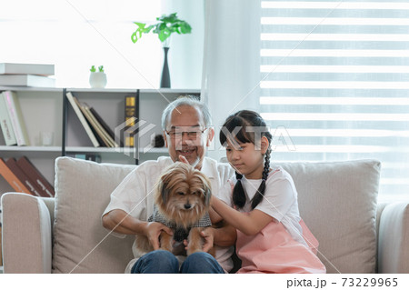 Asian Elderly and children sit on sofa and playing with dog together in living room at home Asian Elderly and children sit on sofa and playing with dog together in living room at home 73229965