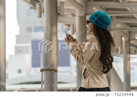Beautiful young woman holding smart phone with green knit hat and standing in a modern city. 73233448