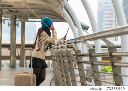 beautiful young woman holding a tablet with green knit hat and standing in a modern city. beautiful young woman holding a tablet with green knit hat and standing in a modern city. 73233449