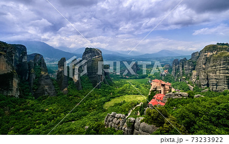 View over nunnery of Moni Agias Varvaras Roussanou, rocks of Meteora, Greece and valley. UNESCO World Heritage. Cloudy sky, sun rays fall on monastery View over nunnery of Moni Agias Varvaras Roussanou, rocks of Meteora, Greece and valley. UNESCO World Heritage. Cloudy sky, sun rays fall on monastery 73233922