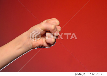 Human hand that squeezed fingers into a fist, symbolizing hatred and resistance, isolated on a red background 73235076