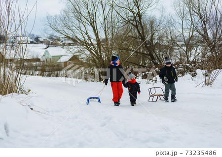 Three children are dragging sleigh in the mountain 73235486