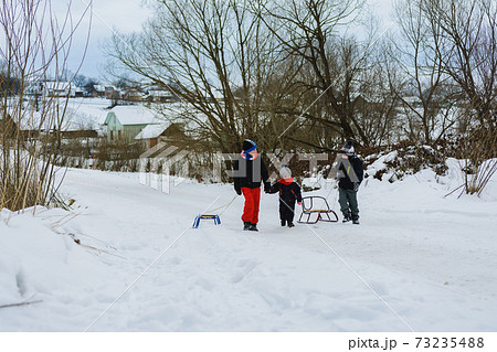 Three children are dragging sleigh in the mountain 73235488