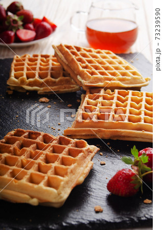 Homemade Belgian waffles on slate tray with maple syrup and strawberries aside Homemade Belgian waffles on slate tray with maple syrup and strawberries aside 73239590