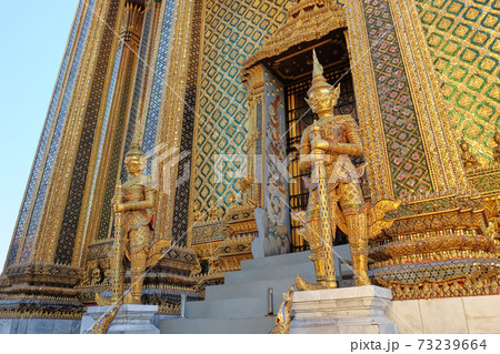 Two gilded sculptures of warriors guard the entrance to the magnificent Buddhist temple. 73239664