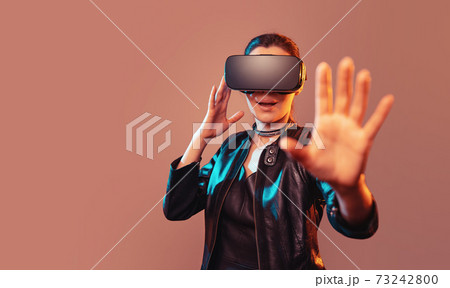 Young girl getting experience VR headset is using augmented reality eyeglasses being in virtual reality. Girl with hands up wearing virtual reality goggles. Woman touching air during VR experience Young girl getting experience VR headset is using augmented reality eyeglasses being in virtual reality. Girl with hands up wearing virtual reality goggles. Woman touching air during VR experience 73242800
