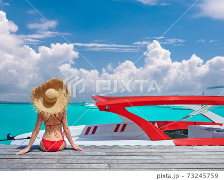 Woman in bikini sitting on jetty with boat Woman in bikini sitting on jetty with boat 73245759