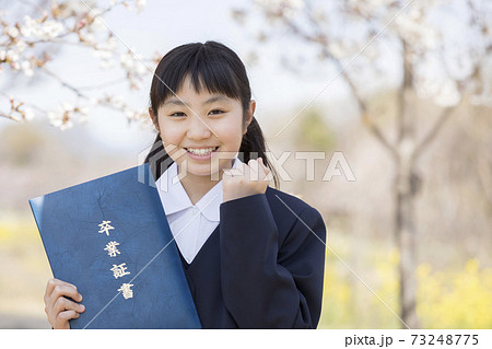 桜の前で卒業証書を持つ制服姿の女子小学6年生 卒業イメージの写真素材