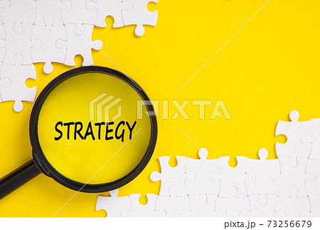 Top view of jigsaw puzzle and magnifying glass with Strategy word . Top view of jigsaw puzzle and magnifying glass with Strategy word . 73256679