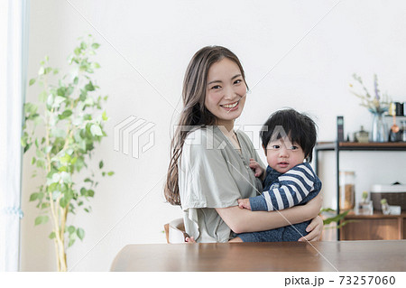 0歳の赤ちゃんを抱えたままパソコンを操作する若い母親の写真素材