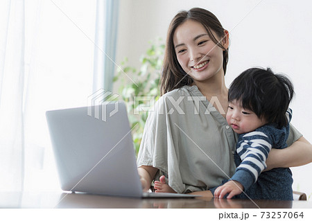 0歳の赤ちゃんを抱えたままパソコンを操作する若い母親の写真素材