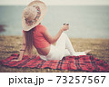 Fashion young lady viewed from back relax and enjoy the ocean view sitting on the field grass with cup of coffee - concept of tourist and spring summer holidays vacation outdoor activity 73257567
