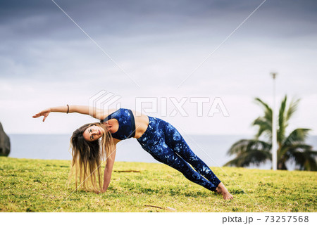 Beautiful young adult woman in balanced pilates exercise position outdoor - sport active people and healthy lifestyle concept - cheerful caucasian female do yoga Beautiful young adult woman in balanced pilates exercise position outdoor - sport active people and healthy lifestyle concept - cheerful caucasian female do yoga 73257568