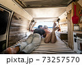Couple lay down on the bed inside a vintage van - summer alternative holiday vacation with young people in love parked in front of a sunny beach and blue free horizon sky 73257570