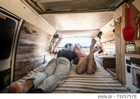 Couple lay down on the bed inside a vintage van - summer alternative holiday vacation with young people in love parked in front of a sunny beach and blue free horizon sky Couple lay down on the bed inside a vintage van - summer alternative holiday vacation with young people in love parked in front of a sunny beach and blue free horizon sky 73257570